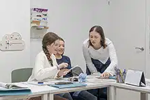 Profesora ayuda a dos alumnas con ejercicio en clase de inglés en academia